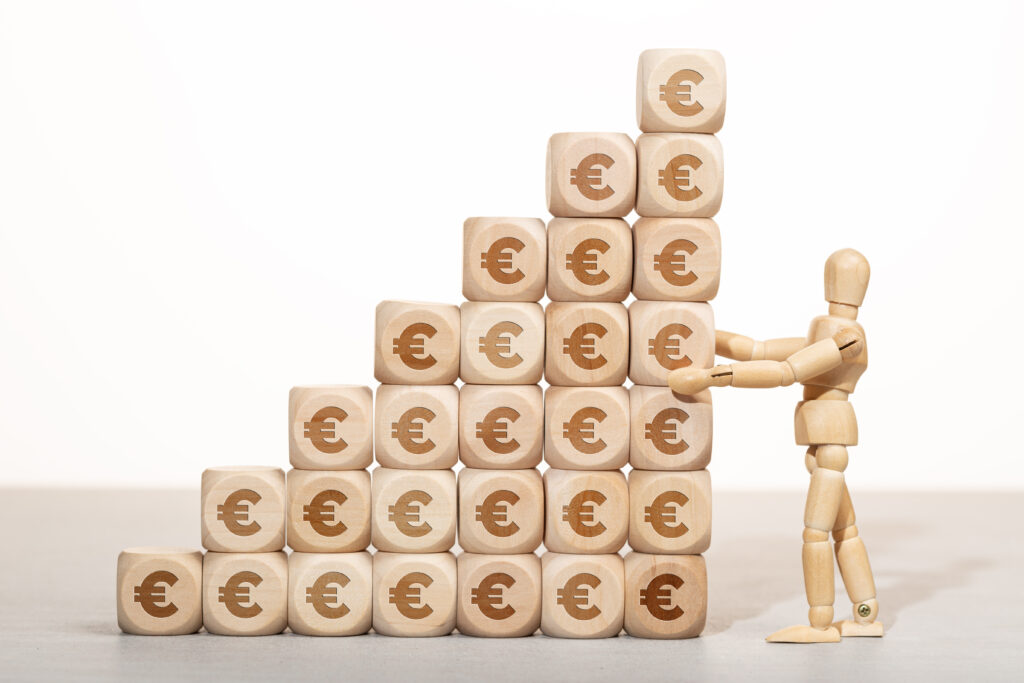 Koncepcja wzrostu, bogactwa lub bogactwa. Drewniany manekin trzymający stos drewnianych klocków ułożonych w stos z symbolem euro