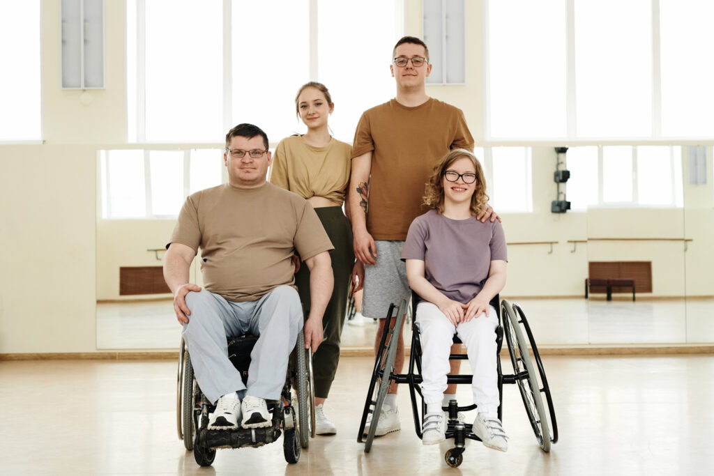 Zdjęcie grupowe dwóch osób niepełnosprawnych na wózkach inwalidzkich i ich partnerów w studiu tańca patrzących w kamerę