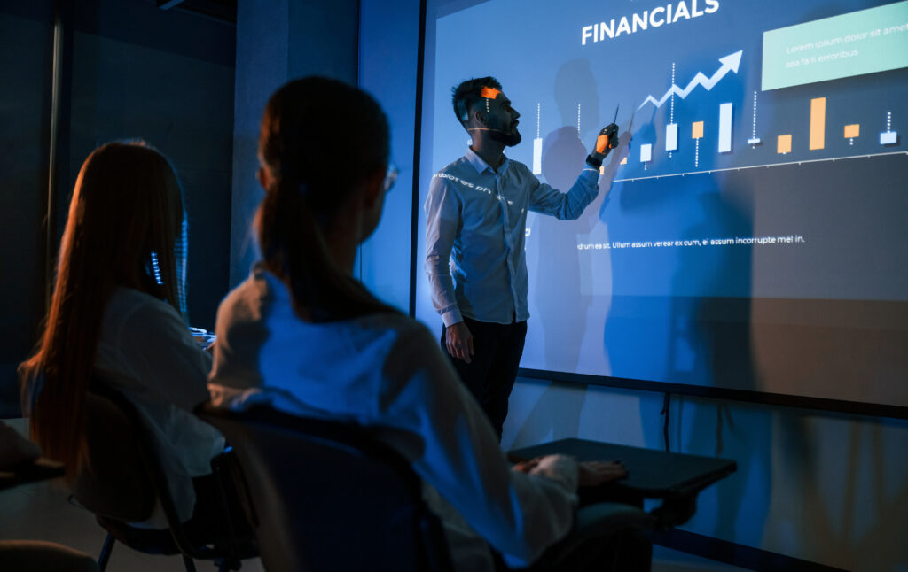 Lider rozmawiający z pracownikami, pokazujący plan na projektorze w biurze spółki giełdowej.