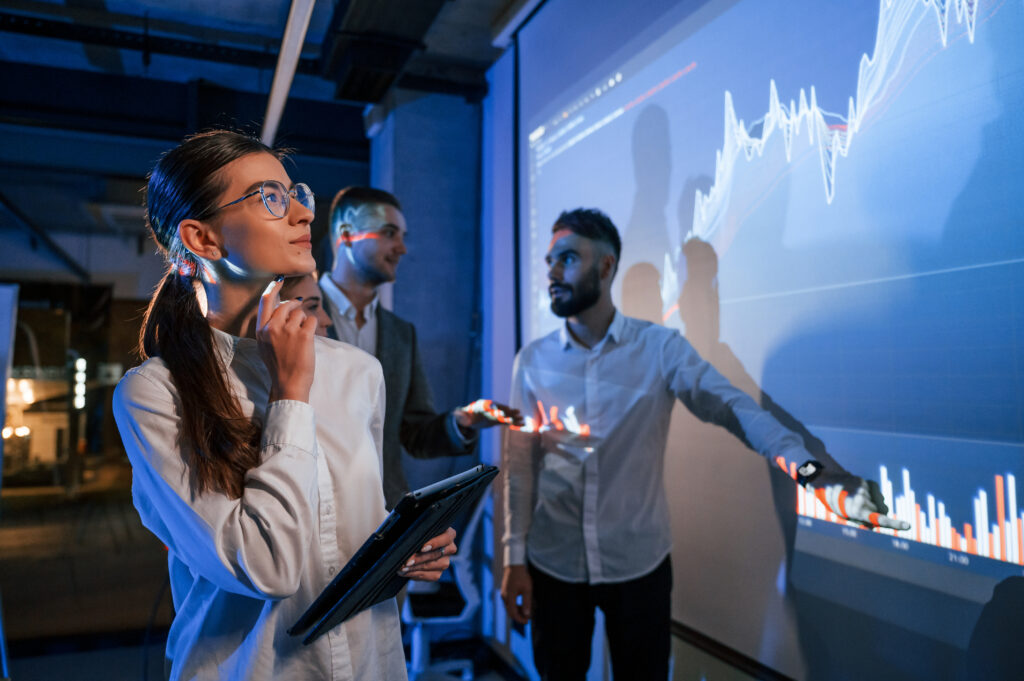 Kobieta stoi z tabletem. Lider rozmawiający z pracownikami, pokazujący plan na projektorze w biurze.